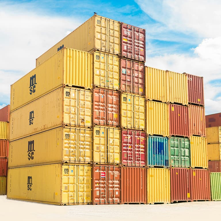 Stacked shipping containers at a busy harbor with cranes and cargo ships, symbolizing global trade and logistics